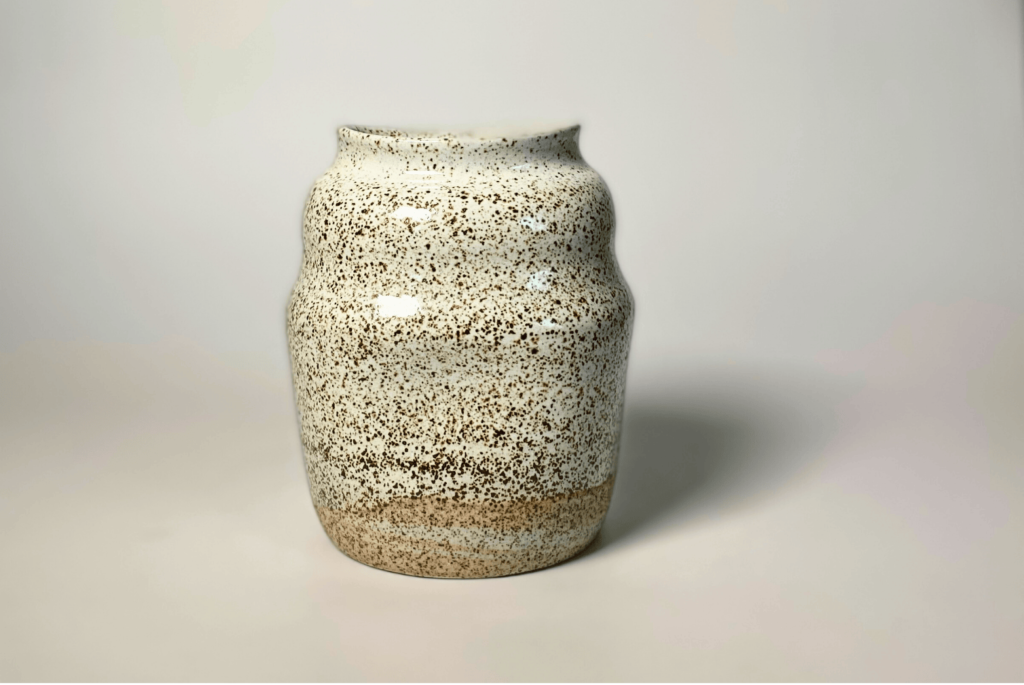 Handcrafted speckled ceramic vase with a natural glaze finish, featuring a rounded silhouette and narrow rim, displayed on a neutral background.